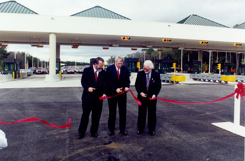 3 men cutting ribbon on road in front of toll plaza