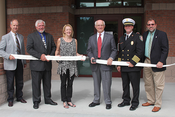 Mayor, Mayor Pro-tem, Town Manager and Fire Chiefs holding fire hose in front of station entrance.
